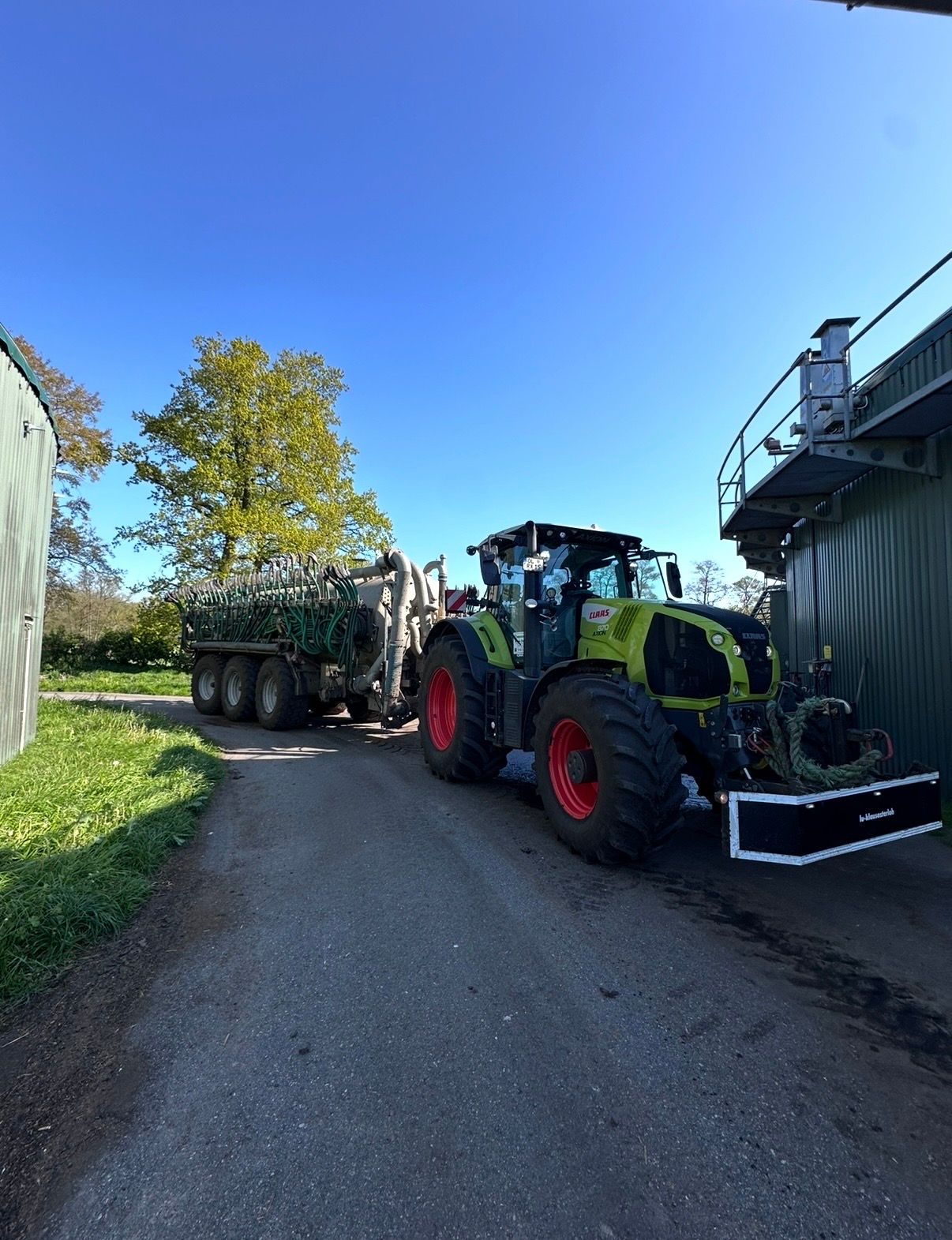 Claas-Schlepper mit Güllefass und eingeklapptem Schleppschlauch-Gestänge am Hof