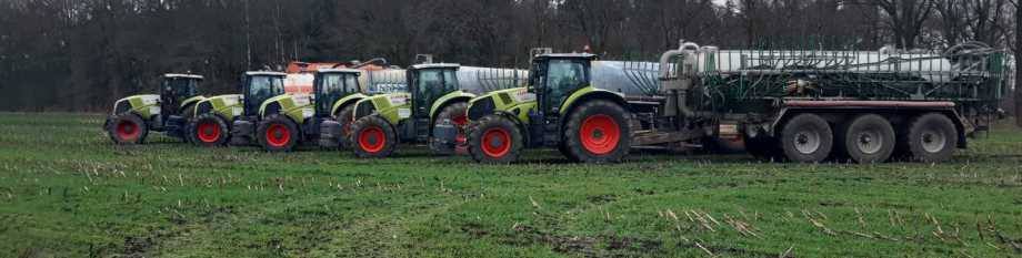 Fünf Claas-Schlepper mit Güllefässern und eingeklappten Schleppschlauch-Gestängen in Reihe am Feldrand
