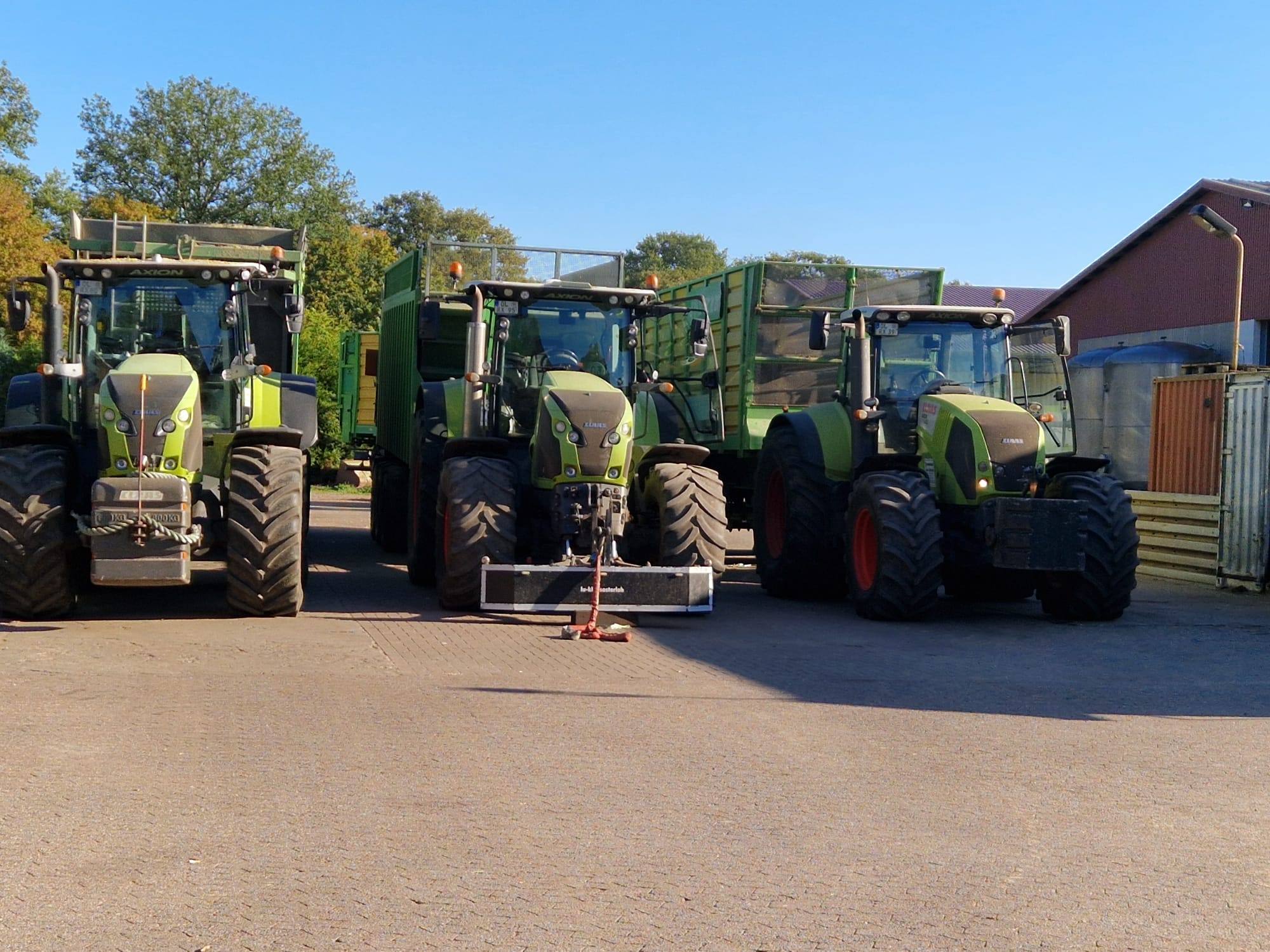 Drei Claas Axion Schlepper und grüne Ladewagen abgestellt auf dem Hof des Lohnunternehmens in Ganderkesee