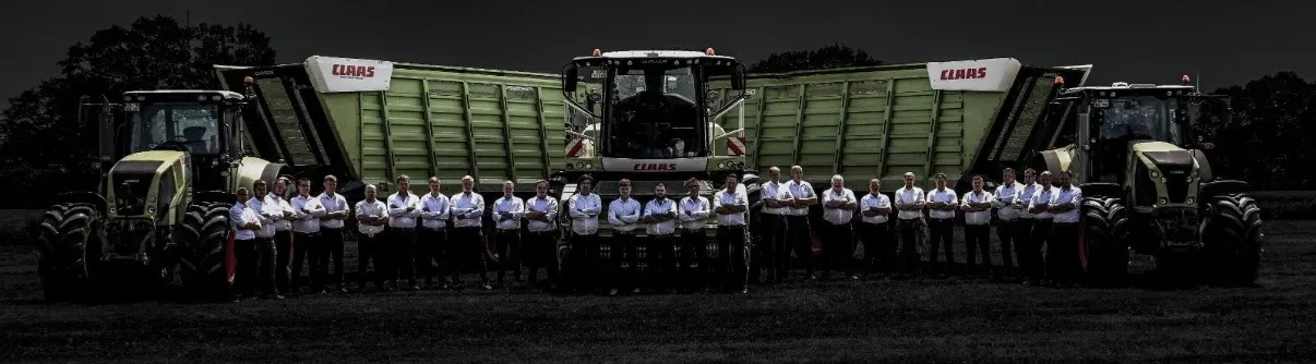 Das Team des Lohnunternehmens Klaus Osterloh aus Ganderkesee steht vor Claas-Häcksler, Ladewagen und zwei Claas-Schleppern auf dem Feld.