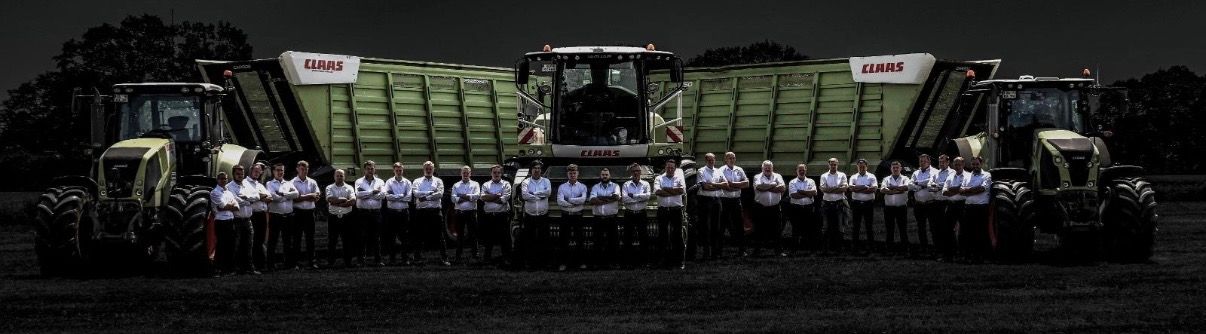 Das Team des Lohnunternehmens Klaus Osterloh aus Ganderkesee steht vor Claas-Häcksler, Ladewagen und zwei Claas-Schleppern auf dem Feld.